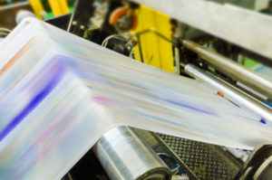 A printing press is producing multiple colors on a long strip of paper.