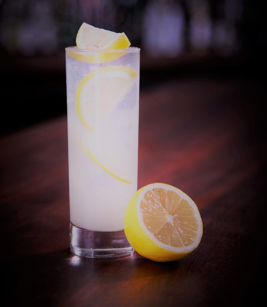 Tall glass of Tom Collins with lemon garnish on a bar counter.