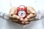 Hands holding a red alarm clock.