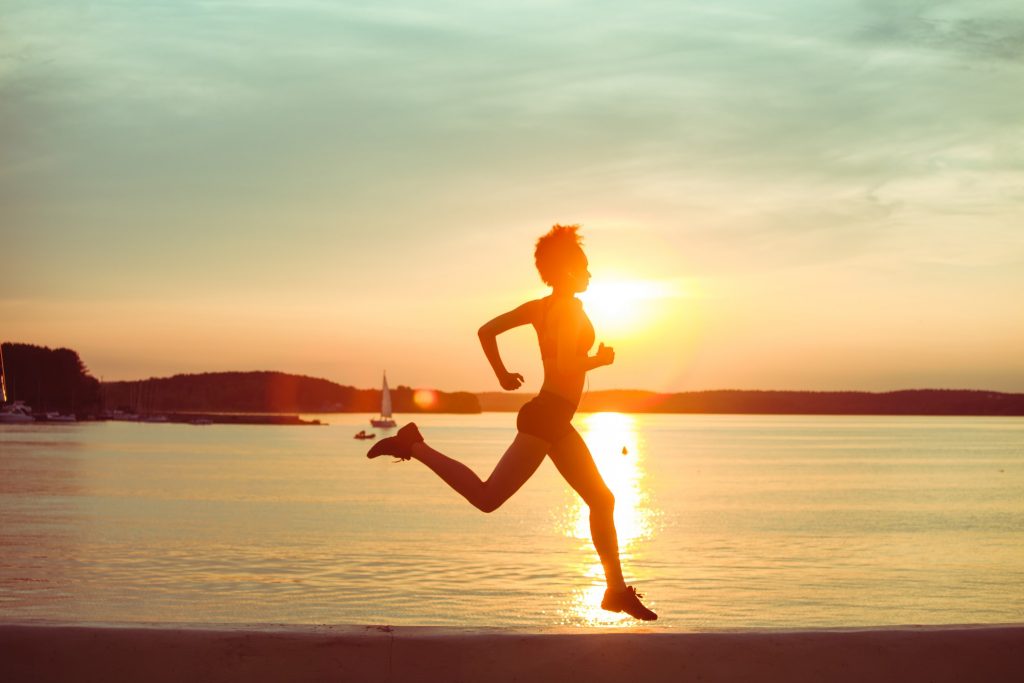 Attractive young African girl athlete running at sunset or sunrise along the beach. Fitness training of runner