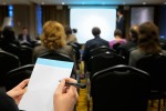 A woman writing in a notebook at a conference.