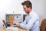 A man holding his wrist in pain over his laptop.