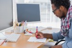 A man doodling on paper in front of two computers.