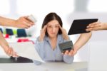 A woman frustrated by four hands holding a calculators, papers, and tablets in her direction.