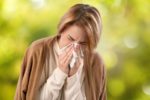 A woman wrapped in a blanket sneezing into a tissue.